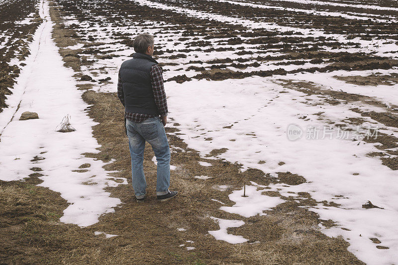 晚冬时节，成年农民站在施肥的农田旁