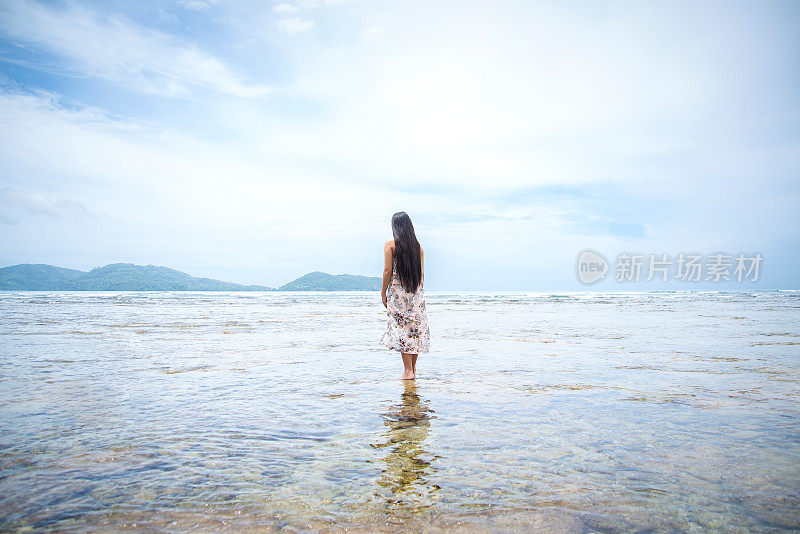 女人站在浅水里望向大海的背影。