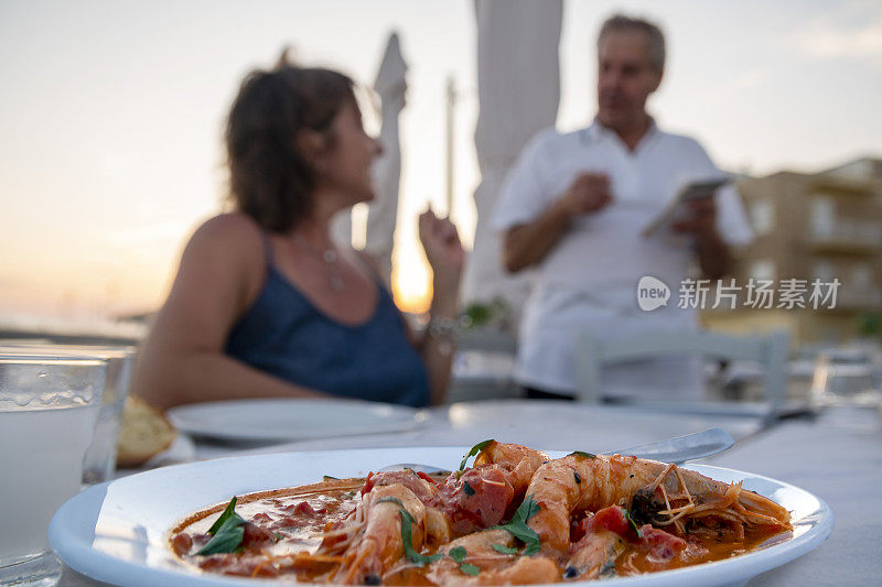 一位希腊妇女正在给服务员点菜，桌上放着美味的鲜虾佐格纳奇