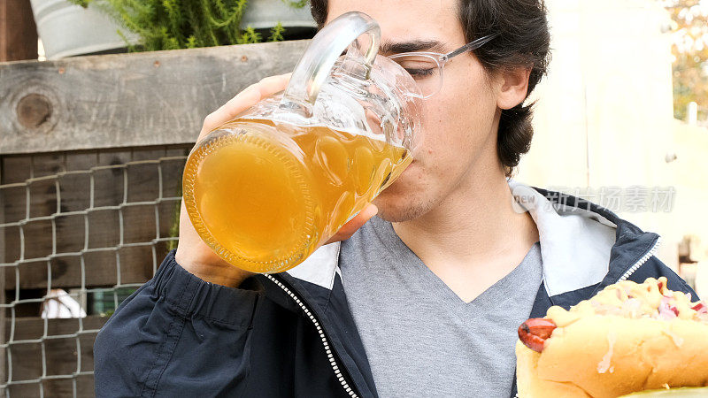 年轻人喝着大杯啤酒，吃着热狗