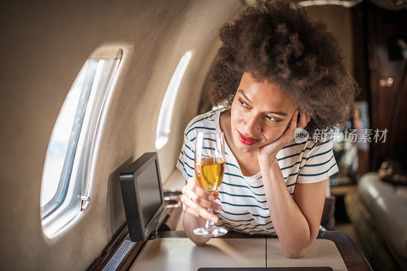一名年轻女子拿着一杯香槟望着私人飞机窗外