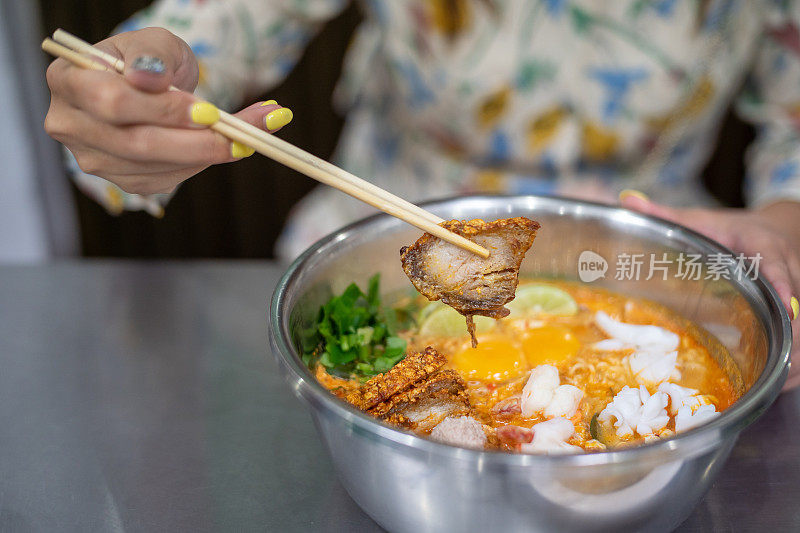 女人拿着烤五花肉，用筷子夹着她的汤面