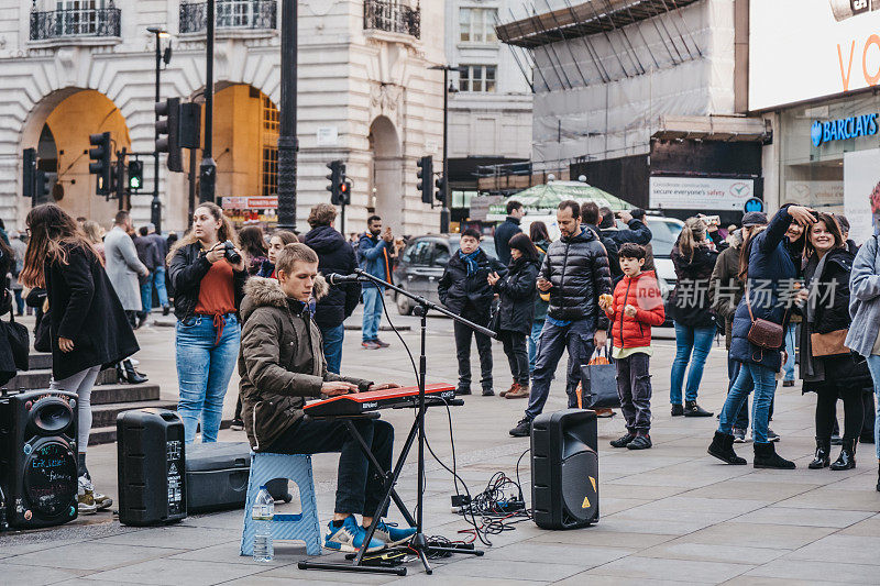 英国伦敦，人们在皮卡迪利广场上观看街头艺人弹奏键盘、唱歌。