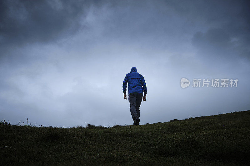 一名男子在阴云密布的天空下攀登斜坡。