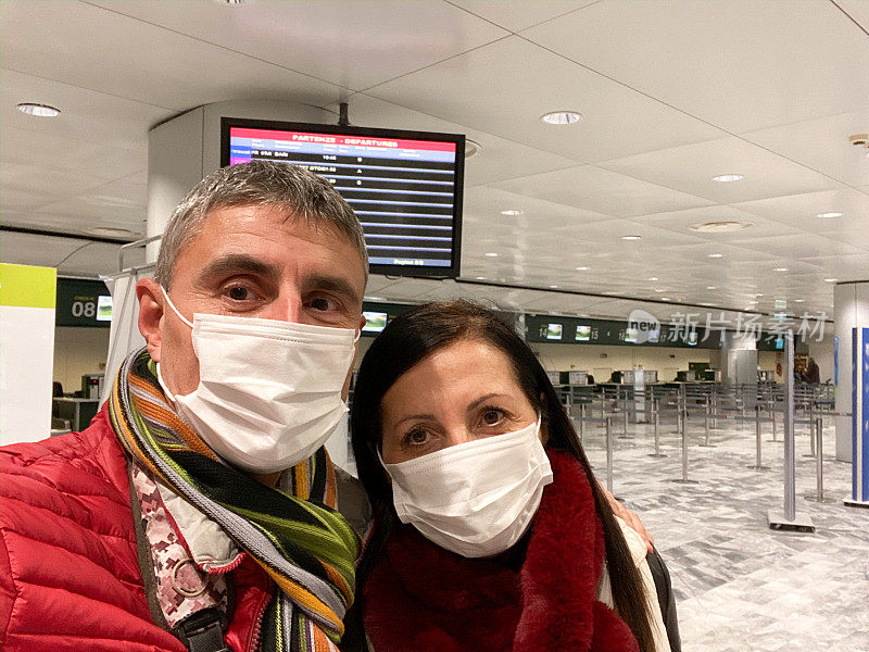 概念、疾病、病毒、过敏、空气污染。欧洲,意大利。一对中年夫妇在机场戴着防护口罩等待登机