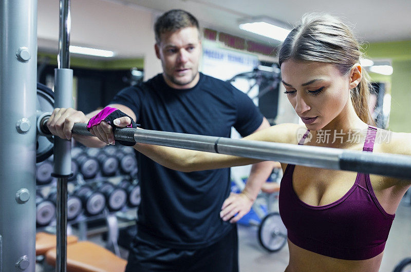 女运动员在健身俱乐部和她的教练进行重量训练