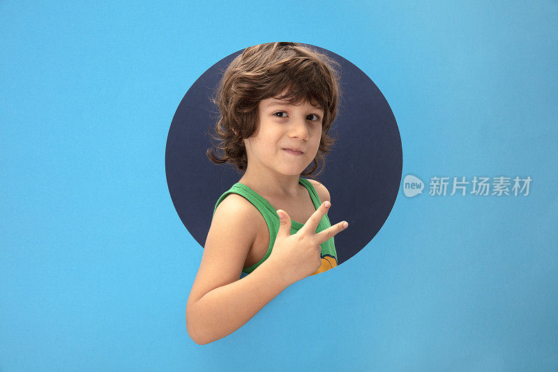 快乐的孩子穿着一件绿色的t恤，双手穿过破纸洞摆出三号的姿势。