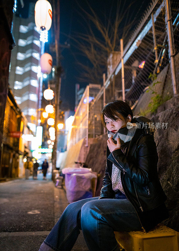 坐在居酒屋酒吧街上的年轻女子