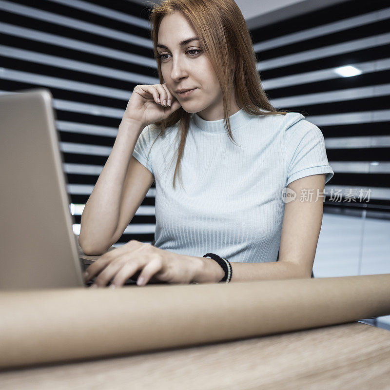 自信有创造力的女商人在她的工作场所，在现代的办公室里用笔记本电脑工作。
