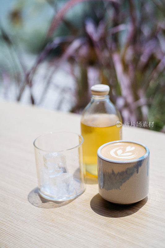 木桌上放着带泡沫的拿铁咖啡和冷泡茶