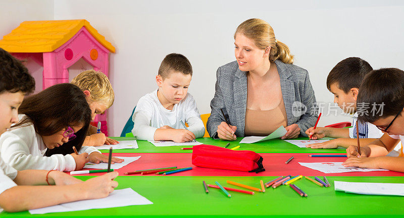 女教师在教室里帮助学生用彩笔画画