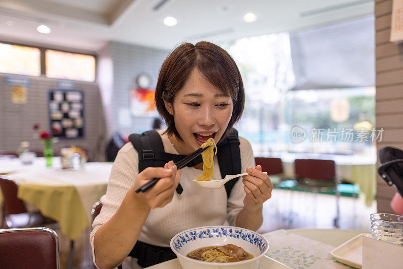 一位年轻的母亲背着她的男婴在餐馆吃拉面