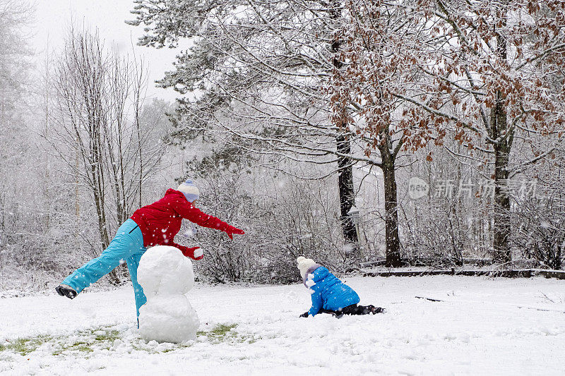 一个白人女孩带着一个孩子，一个5岁的女孩，在他们家的院子里堆雪人和打雪仗。