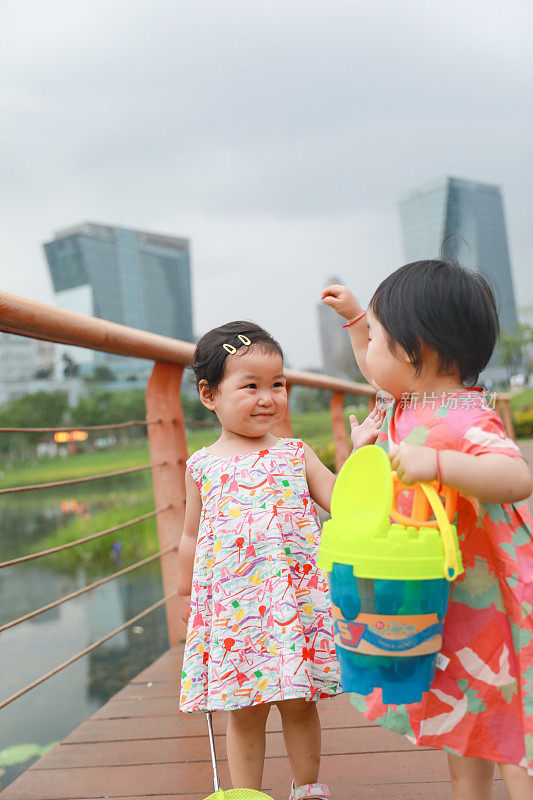 在城市公园里，两个中国女孩在一条建在水池上的红色人行道上玩耍