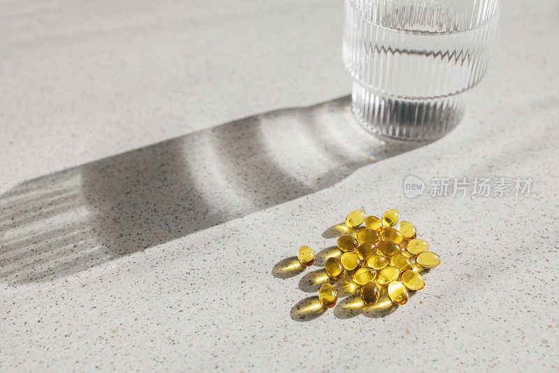 灰色的桌子上放着一堆维生素D药片和一杯水(特写照片)