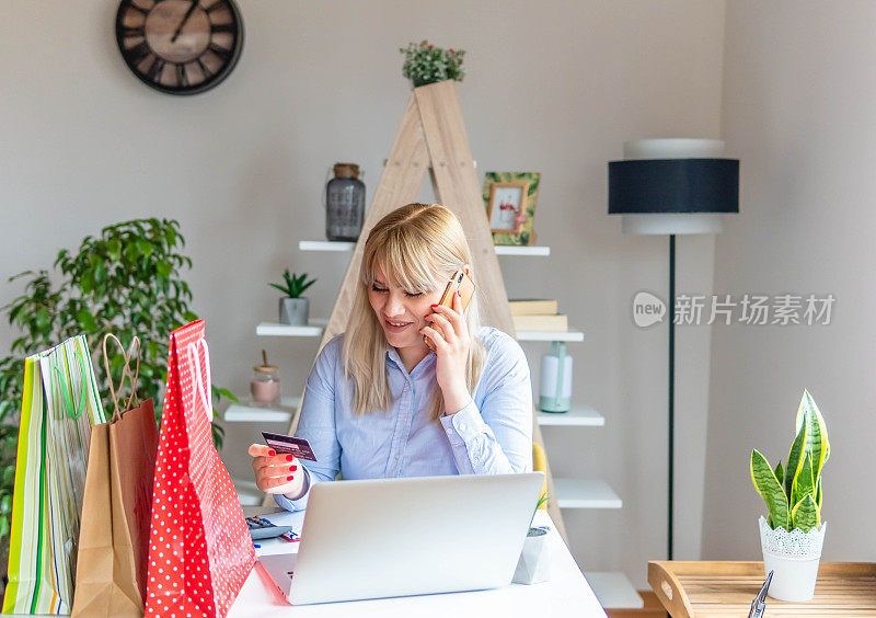 漂亮女人在家里用智能手机在线购物的肖像。坐在家里客厅的桌子上用信用卡购物。居家女性生活方式