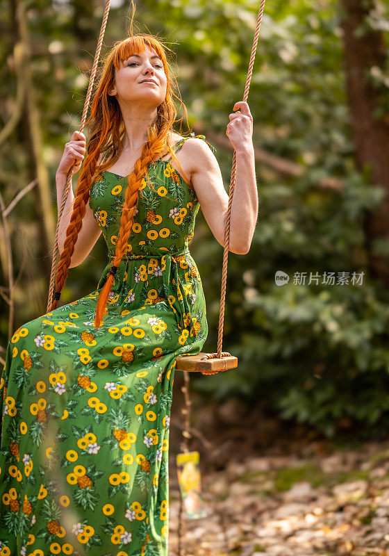 妩媚美丽的年轻女子在公共公园的树林里，荡秋千，穿着绿色的裙子，享受自己