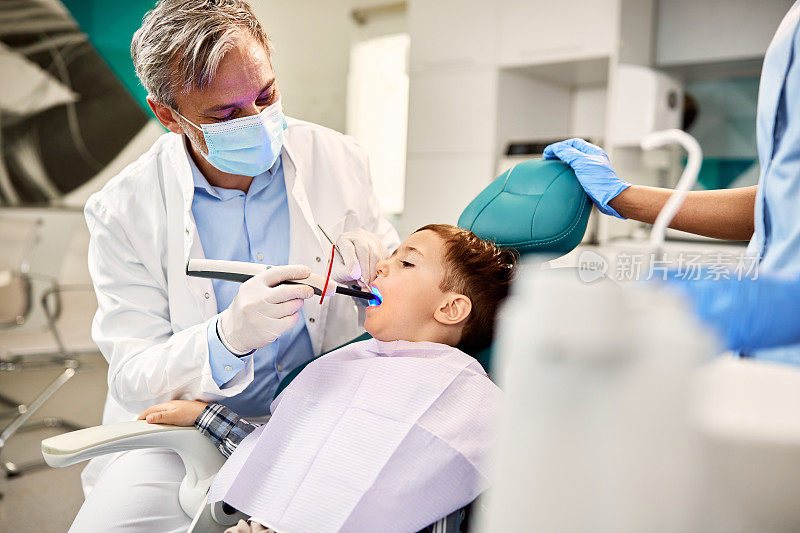 小男孩在牙科预约时，正在用紫外光烘干补牙。