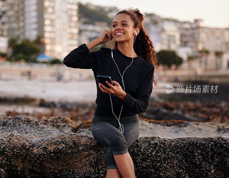 一个迷人的年轻女子在做完瑜伽和听音乐后独自坐在海滩上