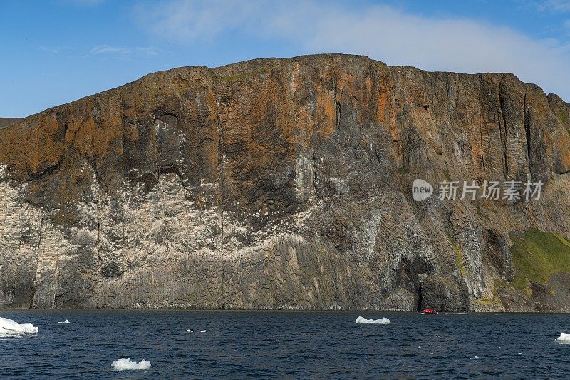 一艘Zodiac摩托化橡皮艇载着从探险游轮上下来的乘客，经过一个峭壁嶙峋的岩石海岸着陆