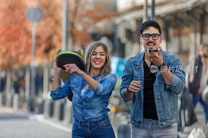 一对年轻夫妇在街上走着，正在用电话。