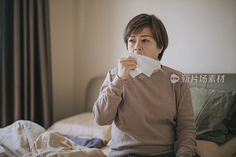 亚洲华人中年妇女用纸巾咳嗽，感觉不舒服，生病在家卧室休息