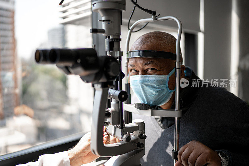 一位戴着防护口罩的长者在诊所接受眼科医生检查的肖像
