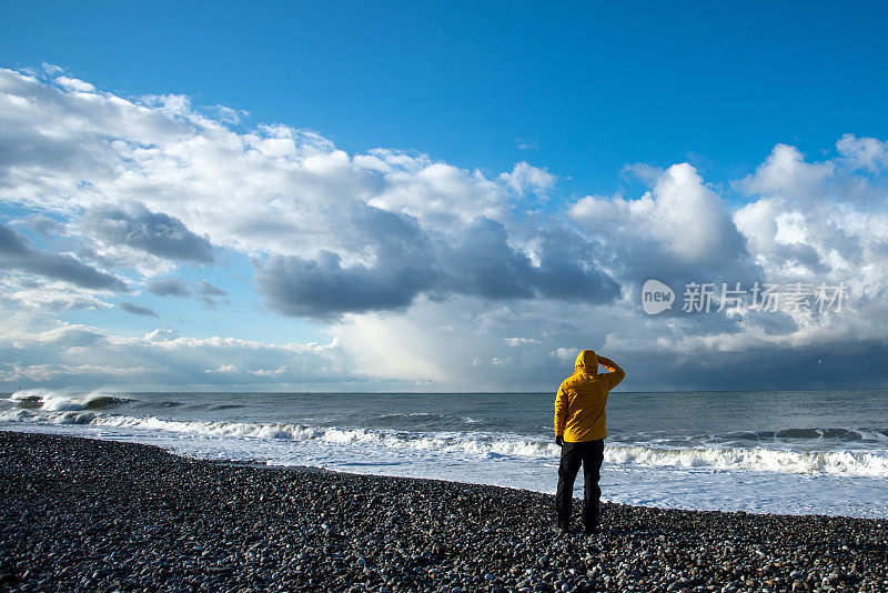 一个穿着黄色夹克的男人在海边的后视图。