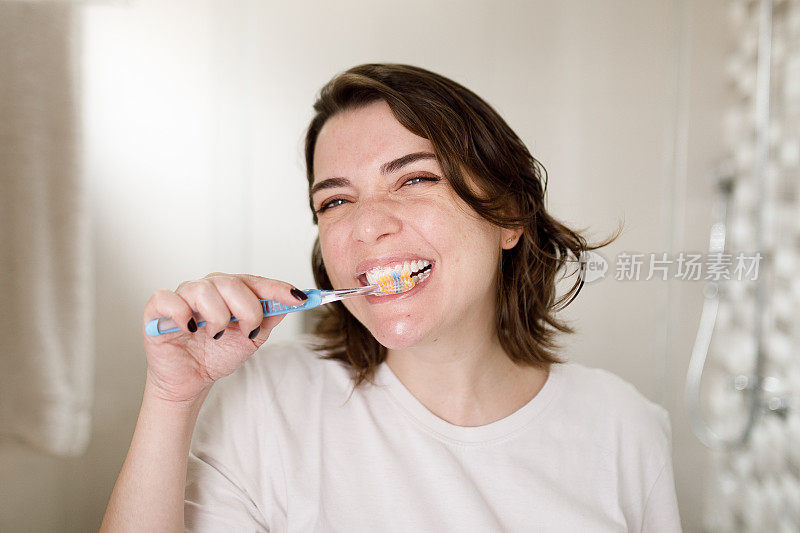 女人一边刷牙一边微笑着看着镜头