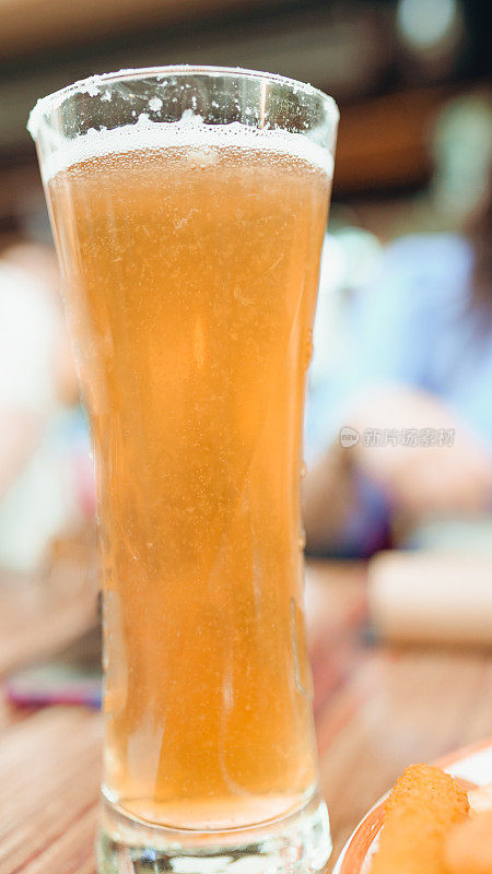 冰冰凉的啤酒，上面有水滴凝结。站在木桌上，背景是酒吧。