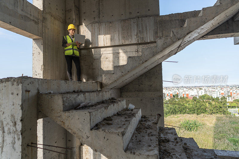 一名亚洲女性建筑工程师在一栋未完工的建筑里用笔记本电脑工作