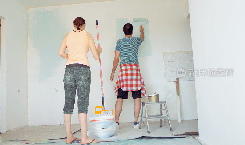 一对夫妇正在粉刷客厅的墙壁