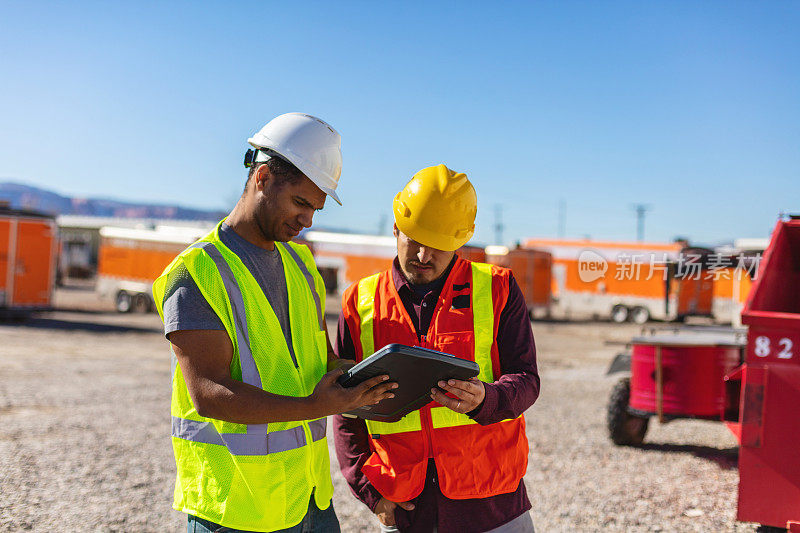 在工地上穿着PPE的黑人和西班牙裔男性建筑工人评估和讨论项目基础设施系列照片