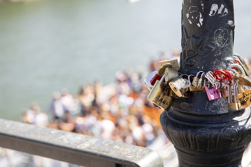 挂锁挂在巴黎艺术桥的灯柱上，一艘观光船从桥下经过