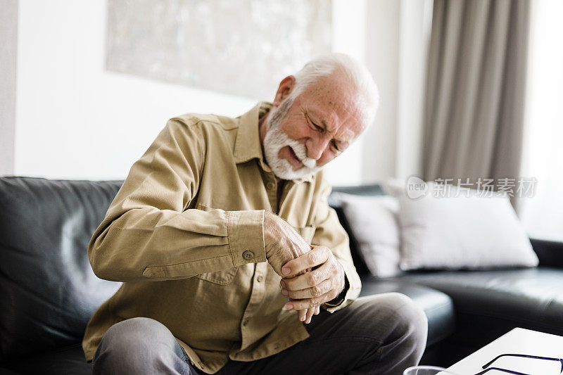 一名老人坐在家里的沙发上，患有关节炎，双手不舒服地搓着。老年人和健康问题的概念，手部疼痛可能是腕管的症状