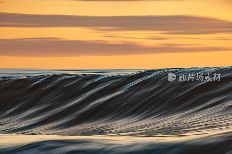 平滑的海浪在清晨形成金色的光和戏剧性的天空在日出