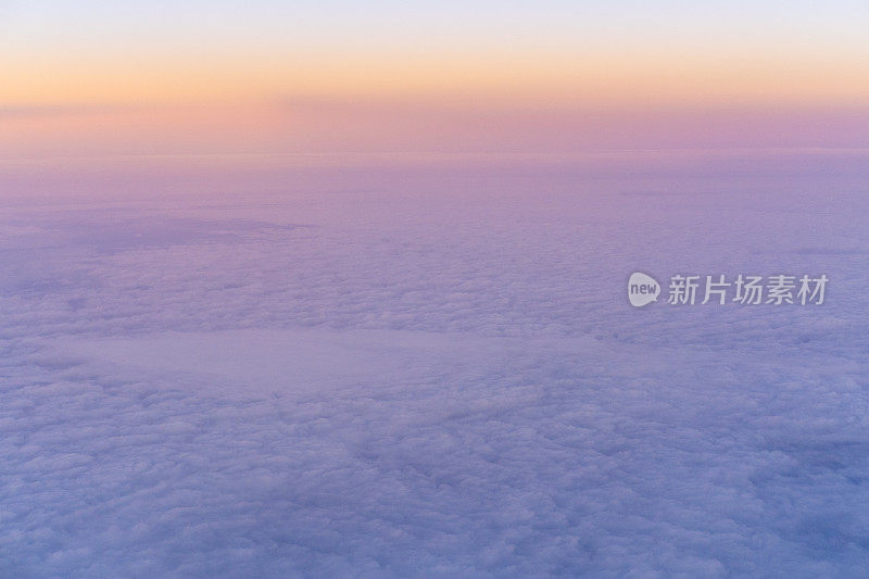 从飞机上俯瞰，淡黄色的日落在粉紫色浓密的云层上，头顶是蓝色的天空
