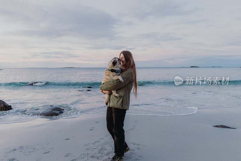 一个女人在海滩上抱着一只可爱的哈巴狗，感觉爱和幸福