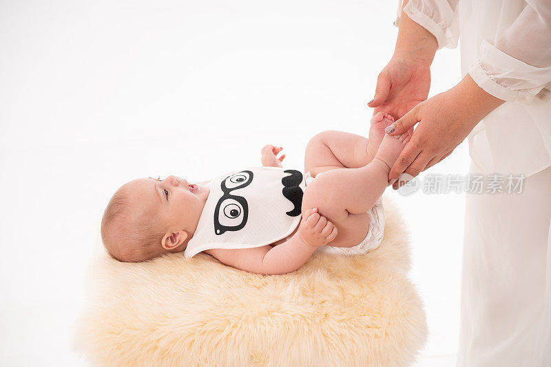 穿着纸尿裤的男婴仰卧在地上，母亲一边抚摸膝盖一边锻炼肌肉。