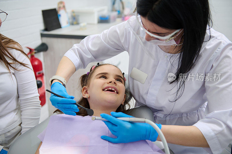 一个快乐的小女孩的肖像，在牙科诊所预约牙医时对她的牙医医生微笑