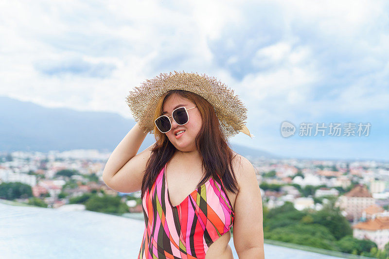 超重的年轻亚洲妇女穿着橙色swimsuitÂ和稻草沙滩太阳帽在游泳池放松快乐加码妇女愉快有趣的假期旅行在夏天。