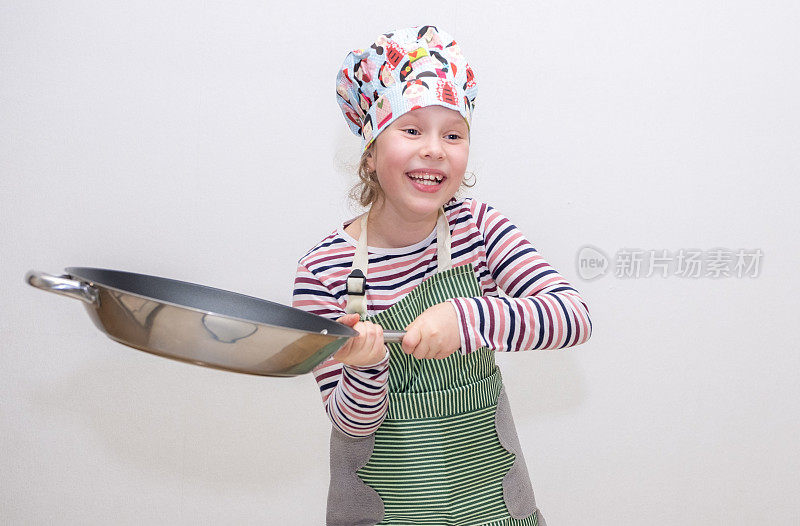 一个白人女孩，8岁，小厨师，手里拿着一个大煎锅，挥舞着煎锅，开心地笑着。在浅色背景上的肖像。