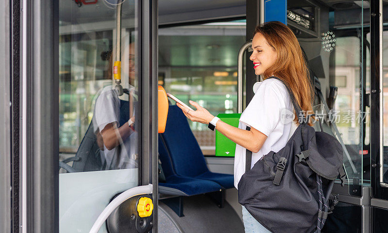 都市年轻女子在电动穿梭巴士内用手机付车费的照片。公共交通移动支付。