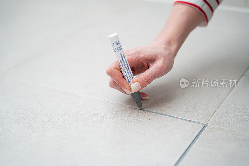 一名妇女用灰色丙烯酸记号笔在地砖接缝处涂浆液，这是家居装修