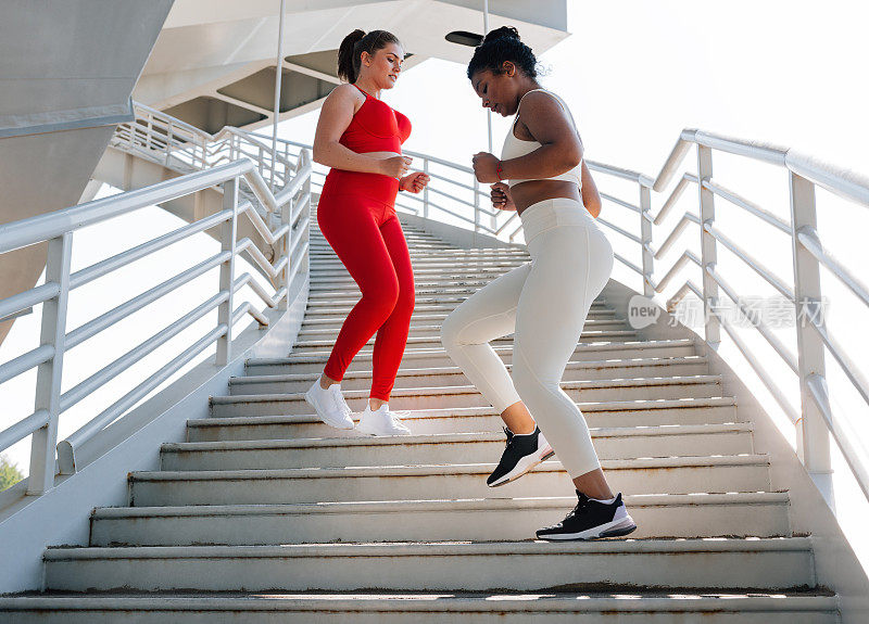 两个女性朋友从楼梯上跑下来。不同体型的女性会一起在户外锻炼。
