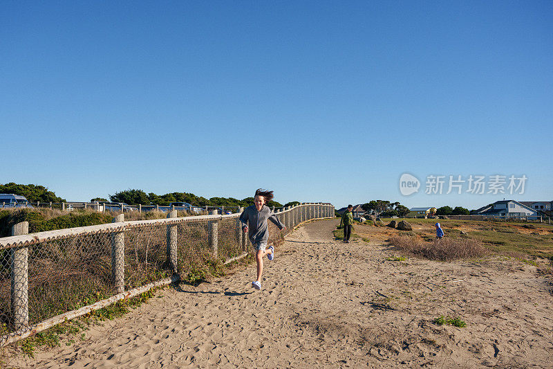 十几岁的男孩沿着沙路跑向海滩