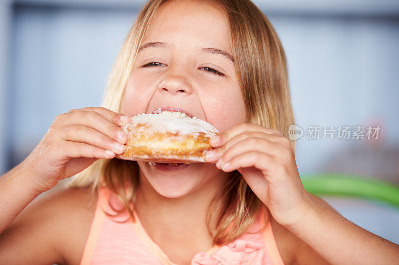 年轻女孩坐在桌边吃甜甜甜圈