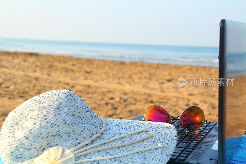 带着太阳帽的笔记本电脑在海滩上