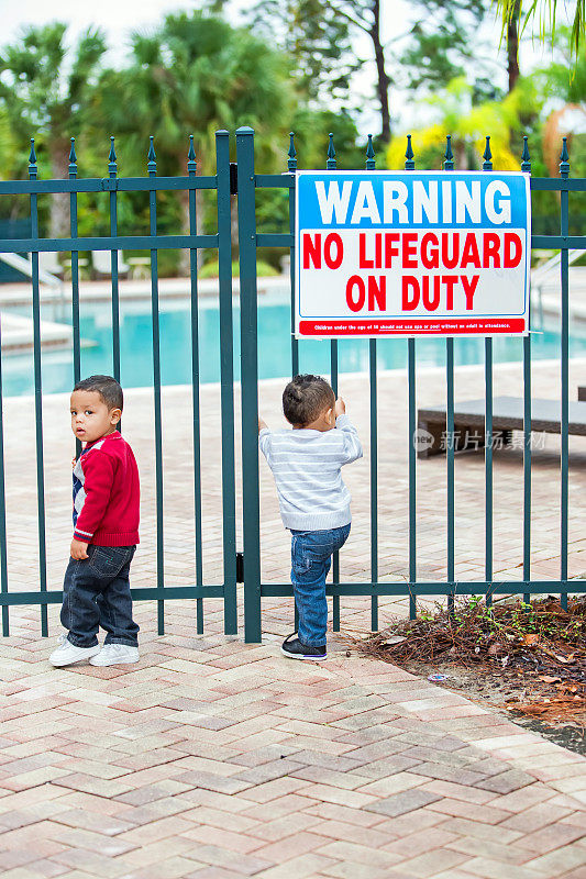 一对黑色双胞胎男孩试图打开锁着的大门进入游泳池