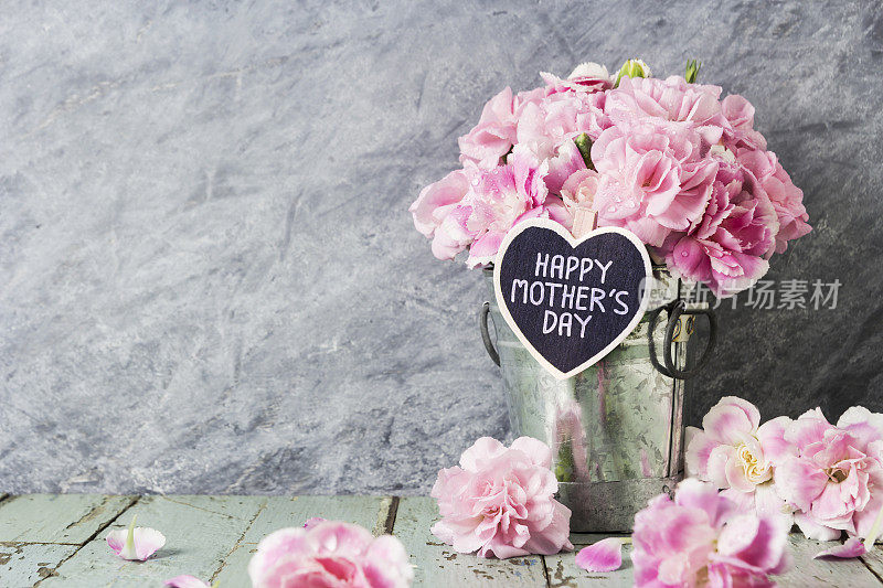 粉红色的康乃馨花装在锌桶里，木头心上挂着母亲节快乐信